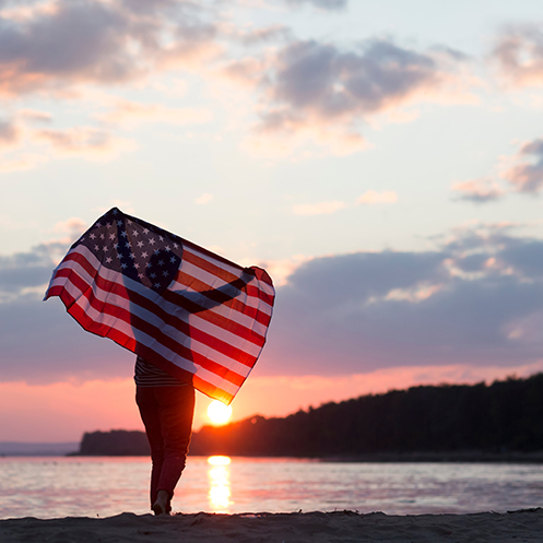 Foto de atardecer y persona sosteniendo bandera de Estados Unidos
