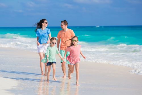 Foto de familia de mujer, hombre y dos niños corriendo felices en la playa