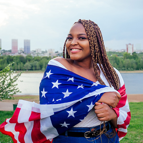 Mujer con bandera de estados unidos alrededor, feliz por haber ganado al lotería de visas