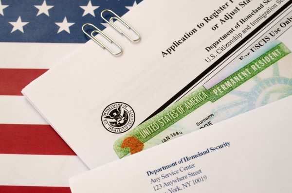 Foto de formulario de visa de residencia permanente de Estados Unidos y bandera del mismo país. 